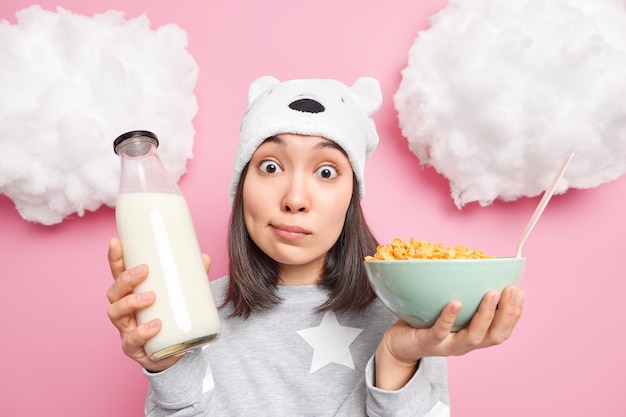 La ragazza guarda con espressione sorpresa la telecamera tiene gli occhi ben aperti indossa il pigiama fa colazione mangia fiocchi di mais con il latte indossa abiti domestici