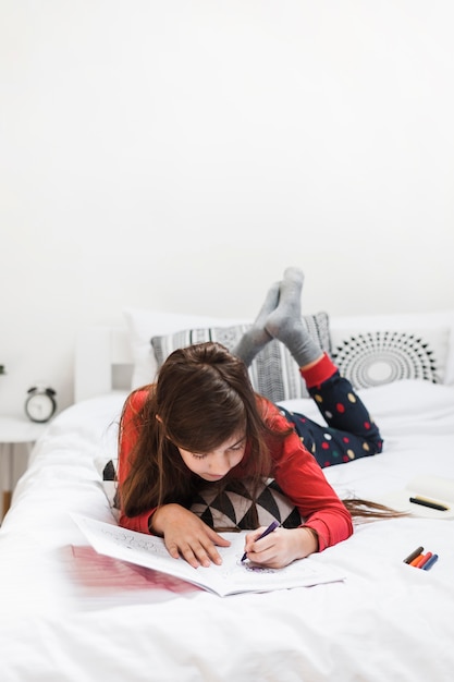 カラフルなクレヨンで描いているベッドに横たわっている女の子