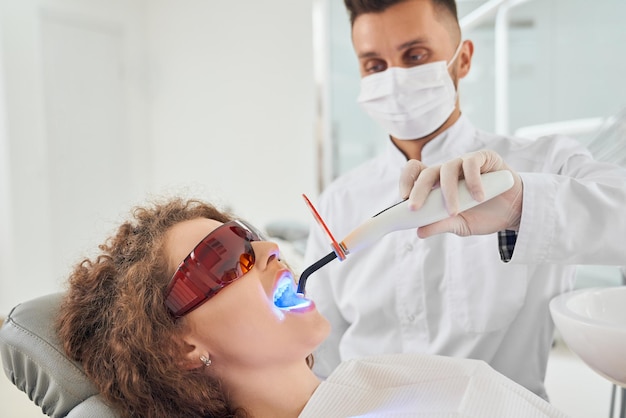 Girl lying on chair while dentist keeping ultraviolet tool