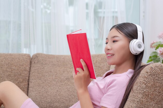 Girl lying on the couch listening to music and reading books.