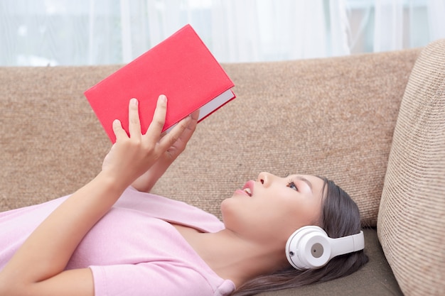 Ragazza sdraiata sul divano ascoltando musica e leggendo libri.