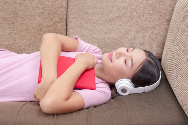 Girl lying on the couch listening to music and reading books.