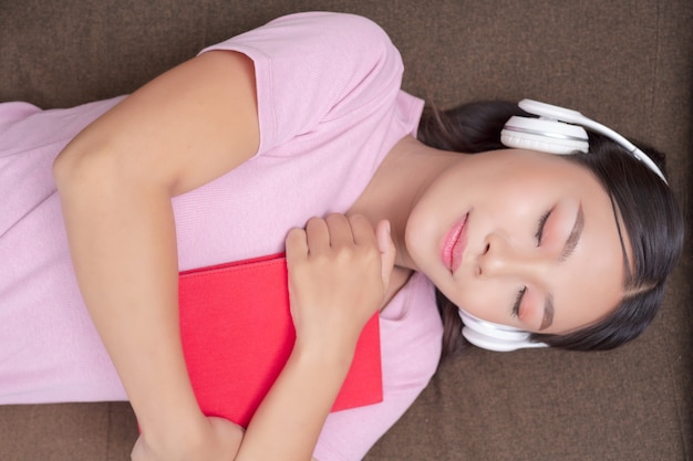 Girl lying on the couch listening to music and reading books.