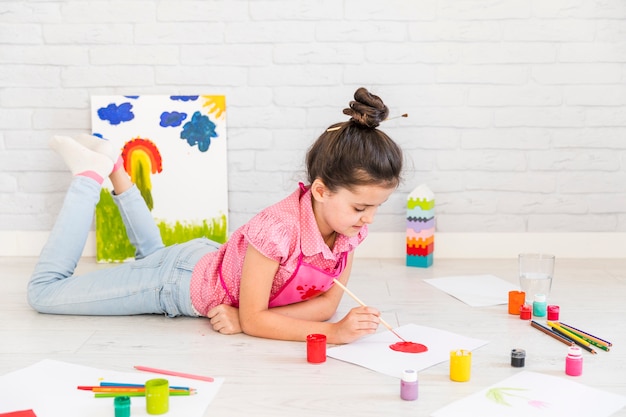 A girl lying on floor painting on white paper with brush