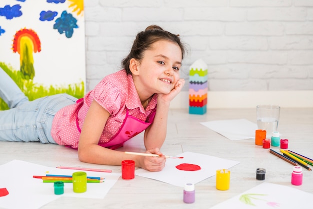 Girl lying on floor painting on white paper with paint brush