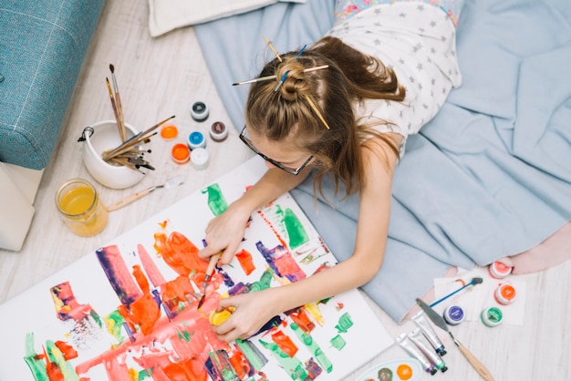 Free photo girl lying on floor and painting with gouache