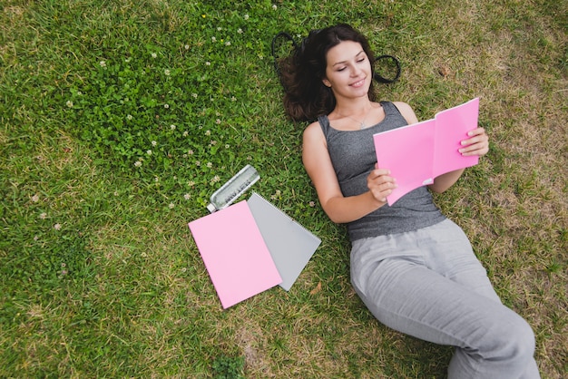 Girl lying on grass reading notebook