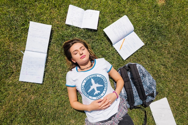 Girl lying on grass surrounded by notebooks