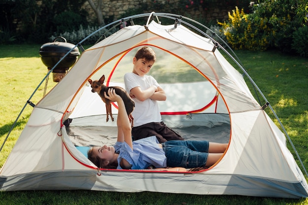 Girl lying and playing with dog in front of her little brother in tent