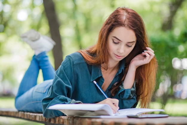 Girl lying on table in park writing