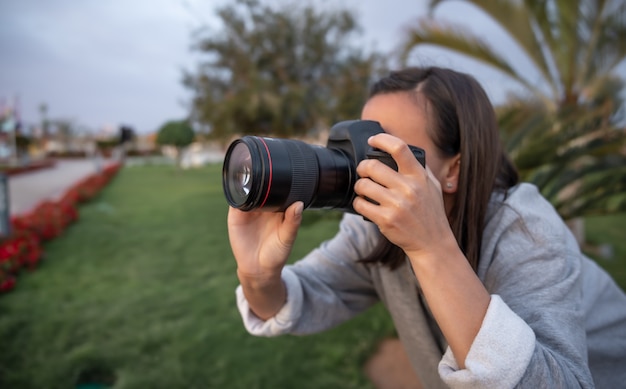 女の子は自然の中で屋外のプロの一眼レフカメラで写真をクローズアップします。