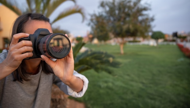 The girl makes a photo on a professional SLR camera outdoors in nature close up.