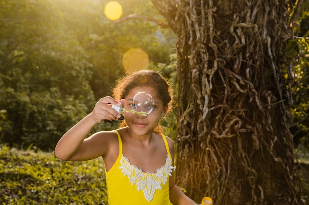 Girl making soap bubble next to tree