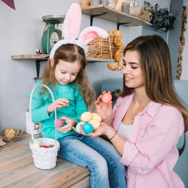 Ragazza e madre che si siedono con le uova di pasqua vicino al canestro