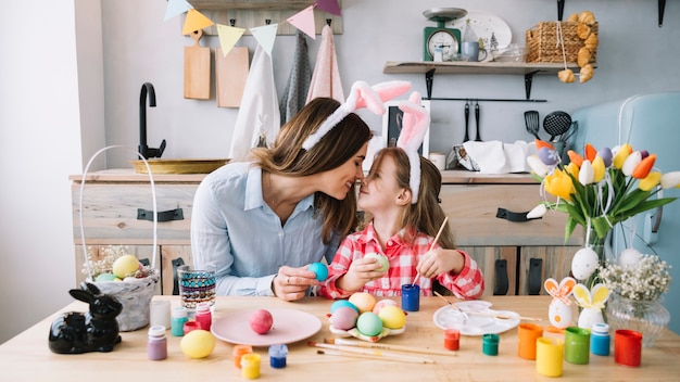 Ragazza e madre che toccano i nasi mentre dipingono le uova per pasqua