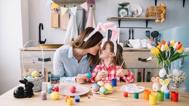 Girl and mother touching noses while painting eggs for Easter