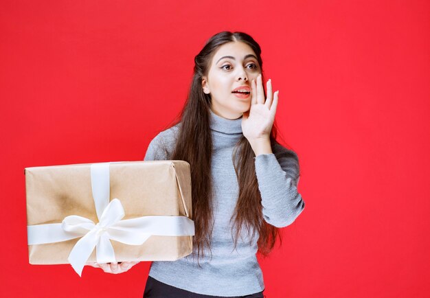 Girl noticing and inviting someone to present a cardboard gift box.