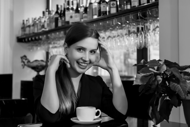 Девушка славянской внешности в баре, кафе или ресторане с белой чашкой. женщина показывает эмоции. молодая очаровательная женщина сидит в баре и пьет кофе или чай в свободное вечернее время