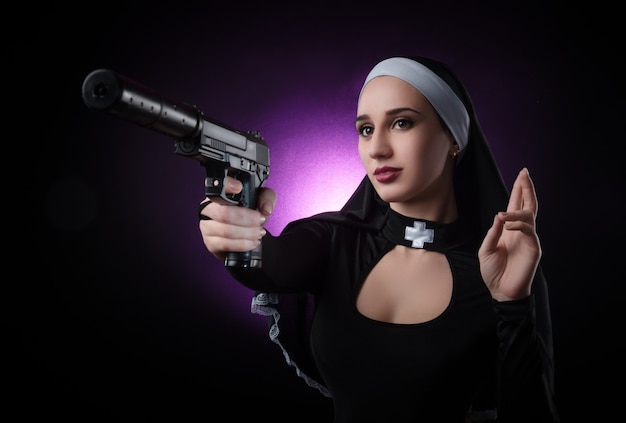 銃でポーズをとって 狙って 射撃する修道女のドレスを着た黒い背景の女の子 プレミアム写真