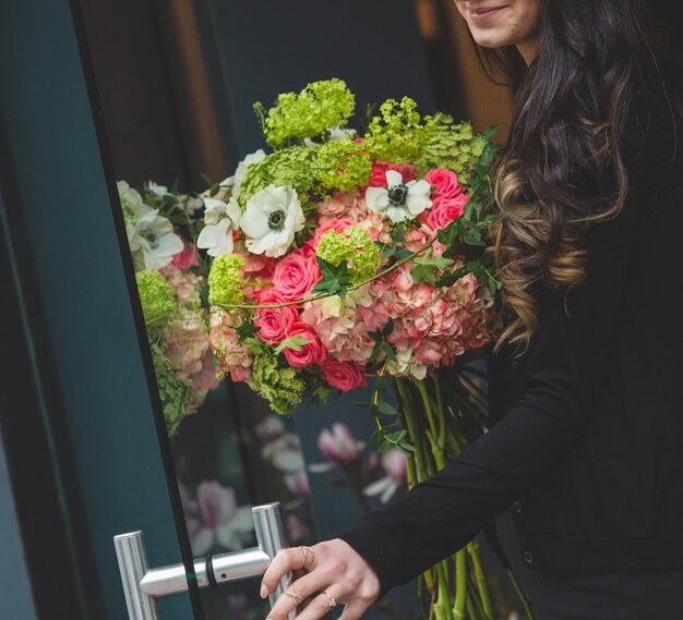 Девушка открывает дверь с букетом из нескольких видов цветов в другой руке