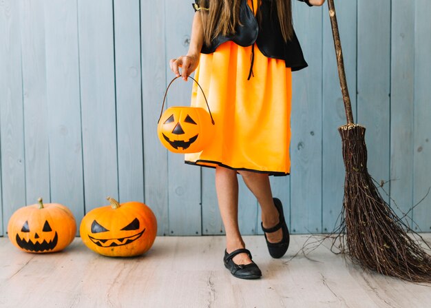 Девушка в оранжевом и черном платье с корзиной Хэллоуина и метлой