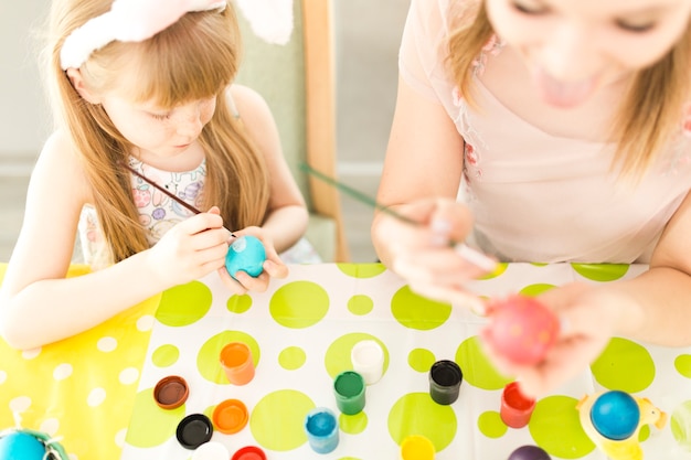 Girl painting Easter eggs with mother