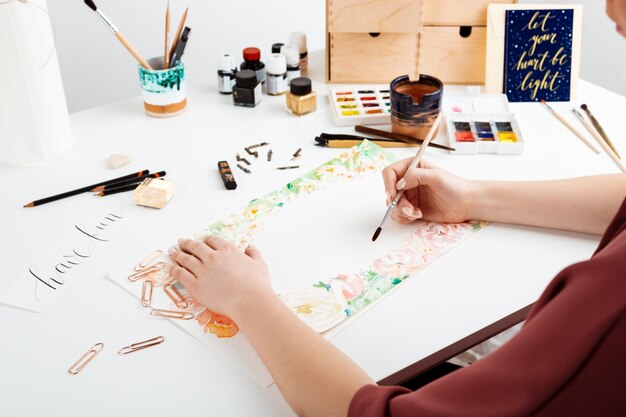 Girl painting flowers on paper with watercolor.