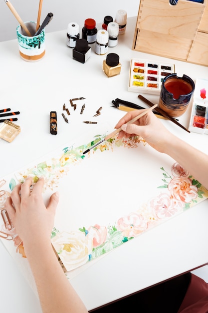 Girl painting flowers on paper with watercolor.