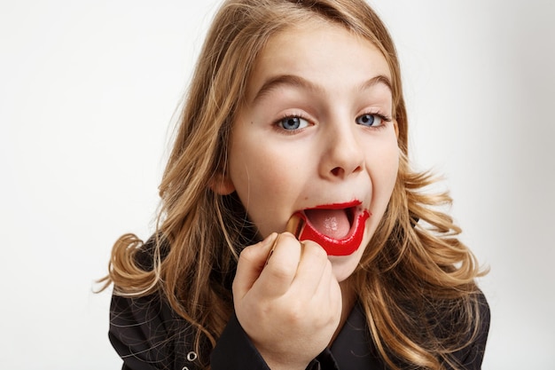 Girl painting lips with open mouth using  mother's red lipstick. dreaming about being adult.