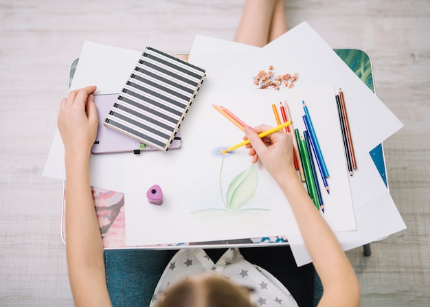 Girl painting on paper at table with set of pencils