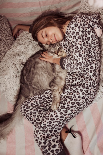 Girl in pajamas hugging her cat and laying on the bed