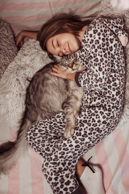 Девушка в пижаме обнимает своего кота и лежит на кровати