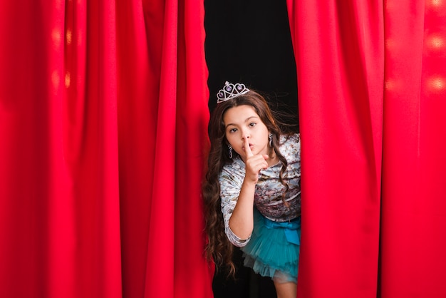 Girl peeking from red curtain making silent gesture