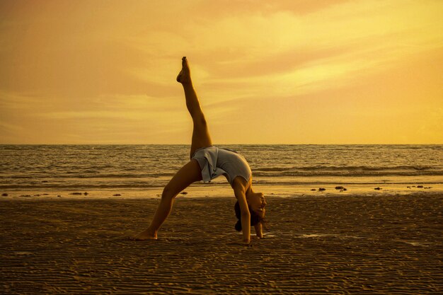 Девушка выполняет акробатические движения на пляже на закате