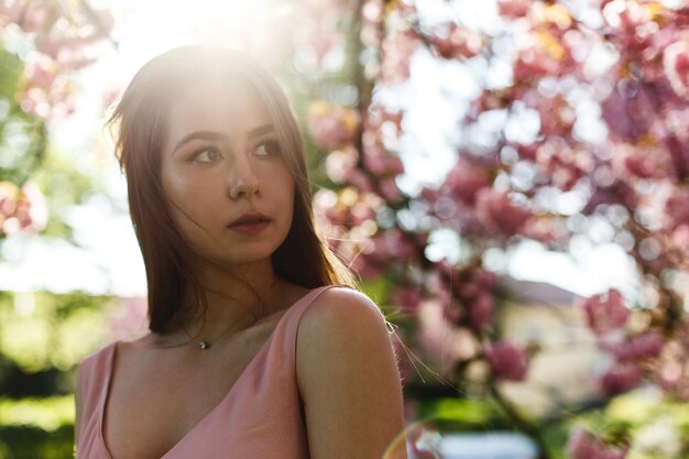 Girl in pink dress stands under blooming sakura tree in the park