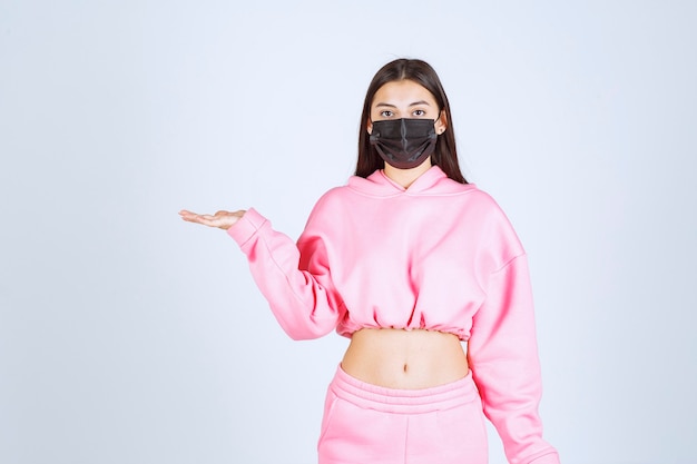 Foto gratuita ragazza in pigiama rosa e maschera nera che punta a sinistra.