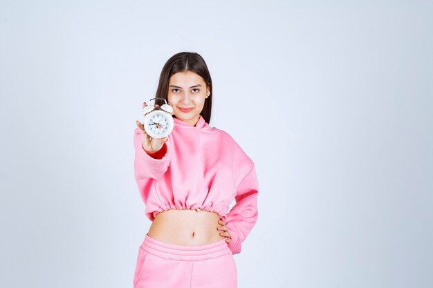 Girl in pink pajamas holding an alarm clock and promoting it as a product. 