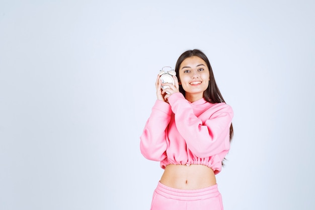 Girl in pink pajamas holding an alarm clock and promoting it as a product. 