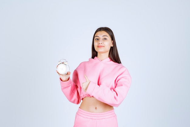 Girl in pink pajamas holding an alarm clock and promoting it as a product. 
