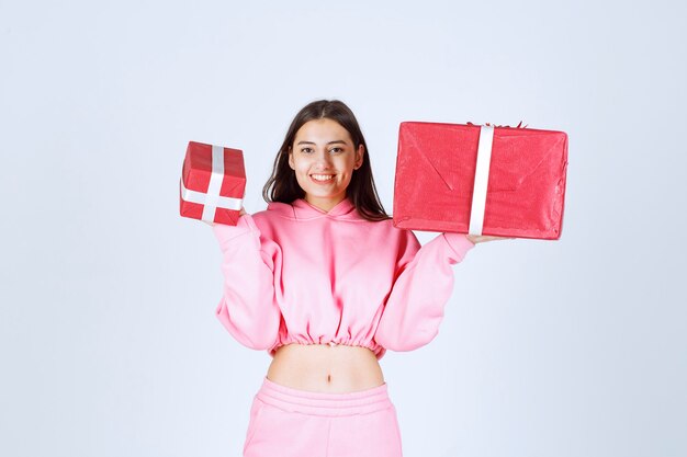 Girl in pink pajamas holding big and small red gift boxes and smiling. 