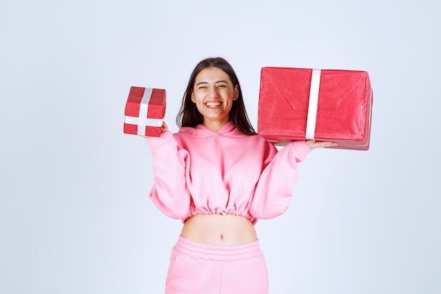 Girl in pink pajamas holding big and small red gift boxes and smiling. 