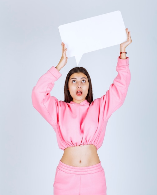 Girl in pink pajamas holding a blank rectangular ideaboard over her head and thinking. 