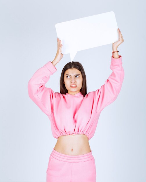 Girl in pink pajamas holding a blank rectangular ideaboard and looks dissatisfied. 