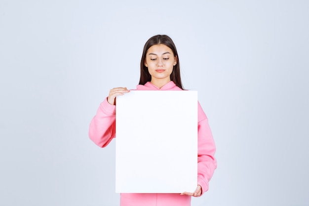 Девушка в розовой пижаме держит перед собой пустую квадратную доску.