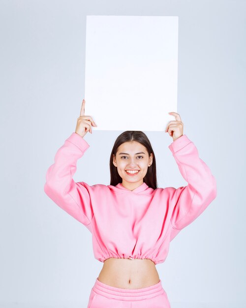 Girl in pink pajamas holding a blank square presentation board over her head to make everyone see it. 