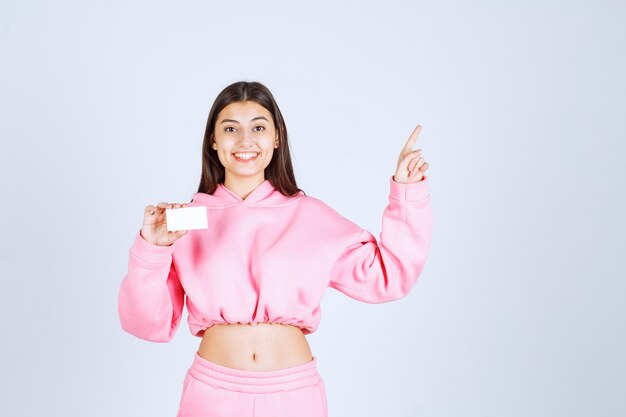 Girl in pink pajamas holding a business card and pointing to someone else. 