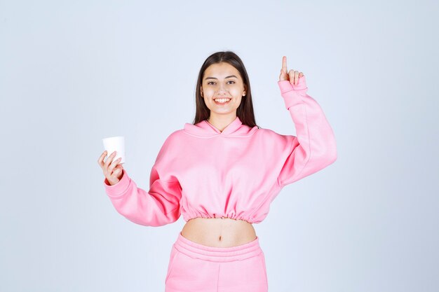 Girl in pink pajamas holding a coffee cup and pointing at something