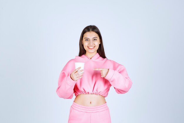 Girl in pink pajamas holding a coffee cup and pointing at something