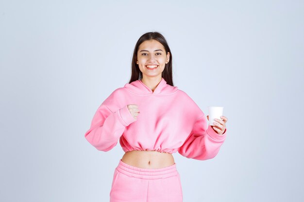 Girl in pink pajamas holding a coffee cup and showing her fist