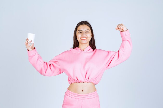 Девушка в розовой пижаме держит чашку кофе и показывает кулак